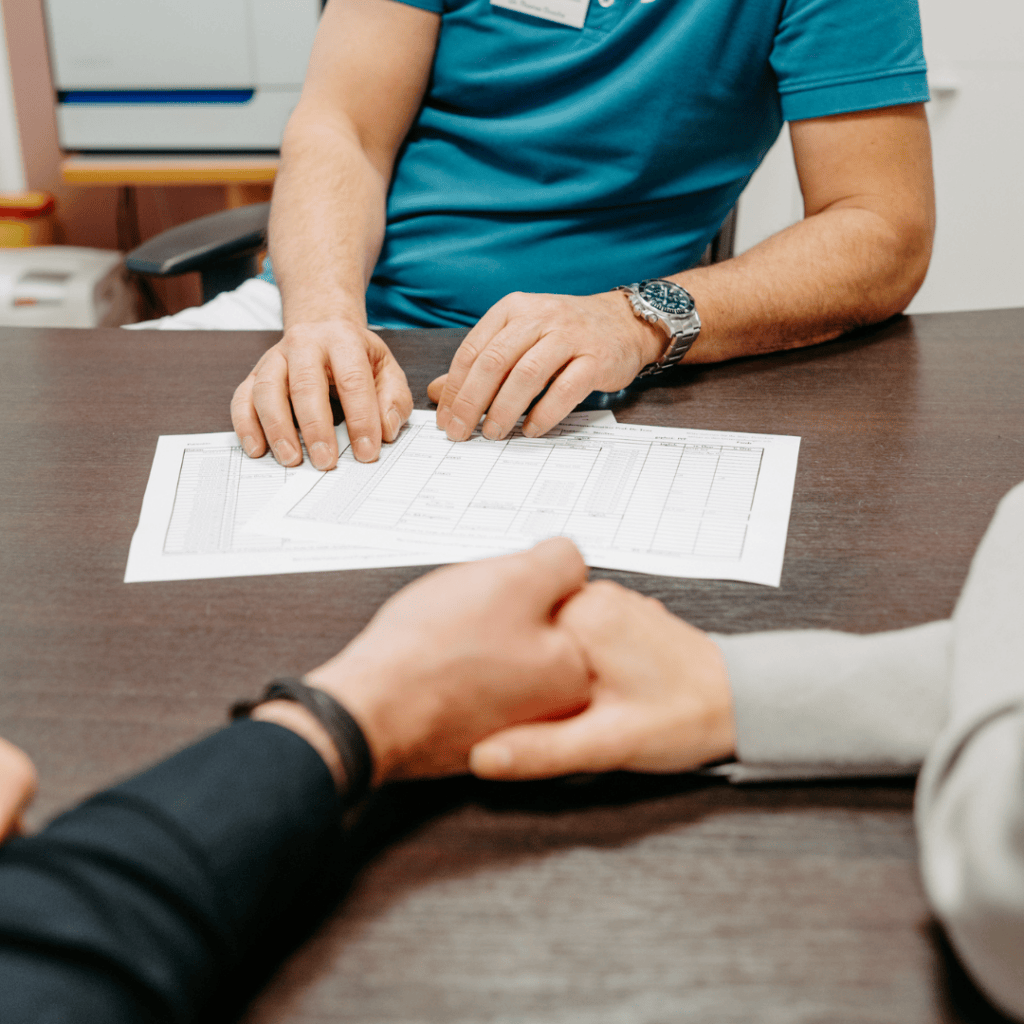 Kinderwunsch-Paar reicht sich die Hände. Gegenüber sitzt ein Kinderwunsch Arzt.